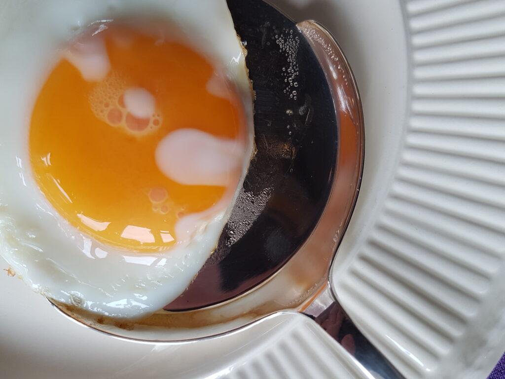 Een gebakken ei op een zilveren spiegeleischep